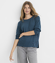 A woman in a teal long-sleeved shirt with lace detailing on the sides stands against a plain gray background. carousel Product Image 1