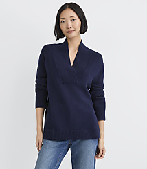 A woman wearing a navy blue V-neck sweater and blue jeans stands against a plain white background. carousel Product Image 1