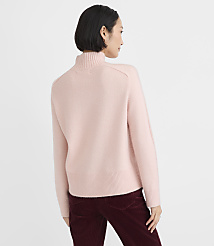 A woman wearing a light pink turtleneck sweater and dark burgundy corduroy pants stands against a plain white background. carousel Product Image 4