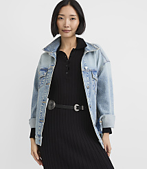 A woman wearing a light-wash denim jacket over a black ribbed dress with a western-style belt stands against a plain white background. carousel Product Image 2