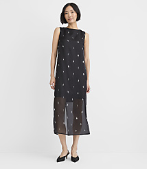 A woman wearing a black sleeveless midi dress with small white patterns and black heels stands against a plain white background. carousel Product Image 1