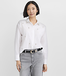 A woman wearing a white embellished button-down shirt and grey jeans stands against a plain white background. carousel Product Image 2