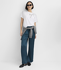 A woman wearing a white t-shirt, teal satin trousers, and sunglasses stands against a plain white background. carousel Product Image 3