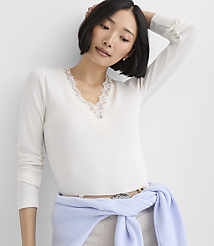 A woman wearing a white lace-trim top and a light blue sweater tied around her waist poses against a plain white background. carousel Product Image 1