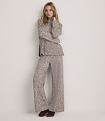A woman wearing a brown and white textured knit two-piece set stands against a plain, light-colored background.