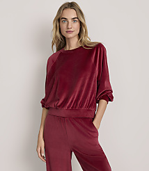 A woman wearing a red velvet two-piece lounge set stands against a plain, light-colored background. carousel Product Image 2