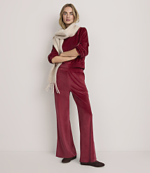 A woman wearing a red velvet two-piece outfit and a cream scarf stands against a plain white background.