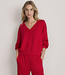 A woman wearing a red v-neck sweatshirt and matching red pants stands against a plain, light-colored background. carousel Product Image 1