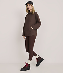 A woman wearing a brown oversized sweater, matching leggings, a black cap, and brown boots stands against a plain, light-colored background. carousel Product Image 1