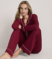 A woman wearing burgundy pajamas with white piping sits on the floor against a plain, light-colored background. carousel Product Image 1