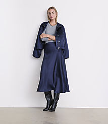 A woman wearing a navy blue jacket, grey top, navy satin skirt, and black boots stands against a plain white wall. carousel Product Image 1