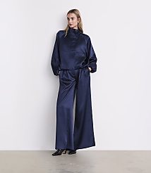 A woman wearing a navy blue satin two-piece outfit and black heels stands against a plain white wall. carousel Product Image 1