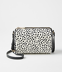 A white and black spotted handbag sits in the foreground against a plain, light gray background. carousel Product Image 1