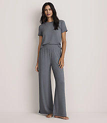 A woman wearing a grey short-sleeved t-shirt and matching wide-leg trousers stands against a plain, light-colored wall. carousel Product Image 1