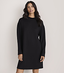 A woman with long dark hair wearing a long-sleeved black dress stands against a plain, light-colored background. carousel Product Image 2