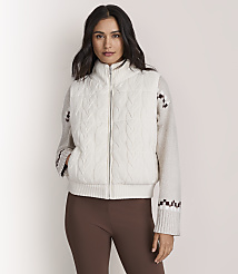 A woman wearing a white cable-knit zip-up sweater and brown leggings stands against a plain, light-colored background. carousel Product Image 1