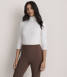 A woman wearing a white turtleneck and brown leggings stands against a plain, light-colored background. carousel Product Image 2