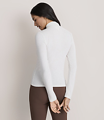 A woman wearing a white long-sleeved turtleneck and brown leggings stands against a plain, light-colored background. carousel Product Image 3