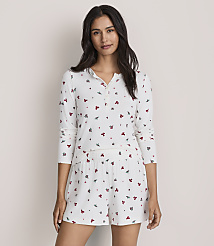 A woman wearing white floral print pajamas stands against a plain, light-colored wall. carousel Product Image 2