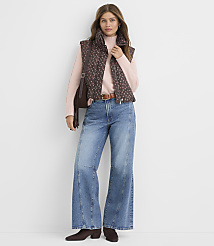 A woman wearing a brown patterned vest, pink sweater, and flared blue jeans stands against a plain white background. carousel Product Image 2