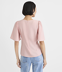 A woman wearing a light pink puff-sleeve top and blue jeans stands with her back to the camera against a plain white background. carousel Product Image 3
