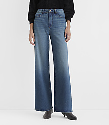 A person wearing a black sweater, wide-leg blue jeans, and black pointed-toe heels stands against a plain light gray background. carousel Product Image 1