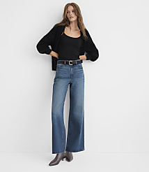 A woman wearing a black cardigan, black top, and wide-leg blue jeans stands against a plain white background. carousel Product Image 1