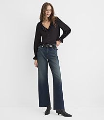A woman wearing a black ruffled blouse and wide-leg blue jeans stands against a plain white background. carousel Product Image 1