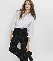 A woman wearing a white pleated shirt and black floral trousers stands against a plain white background. carousel Product Image 4