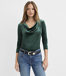 A woman wearing a dark green velvet cowl-neck top and blue jeans stands against a plain white background. carousel Product Image 1