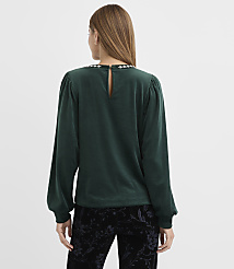 A woman wearing a dark green velvet top and black floral pants stands with her back to the camera against a plain white background. carousel Product Image 3