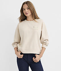 A woman wearing a beige sweatshirt and dark blue jeans stands against a plain white background. carousel Product Image 2
