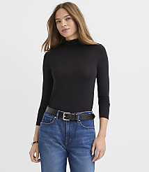 A woman wearing a black turtleneck and blue jeans stands against a plain white background. carousel Product Image 2