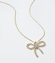 A gold chain necklace with a sparkling bow-shaped crystal pendant rests on a plain white background. carousel Product Image 2