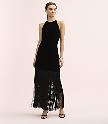A woman wearing a black velvet halter dress with a long fringe skirt stands against a plain light pink background. carousel Product Image 1