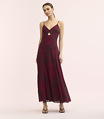 A woman wearing a long, maroon floral-print dress with a cutout detail stands against a plain, light pink background. carousel Product Image 2