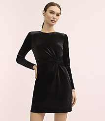 A woman wearing a long-sleeved black velvet dress stands against a plain light pink background. carousel Product Image 2
