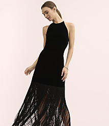 A woman wearing a black velvet dress with a long fringe skirt stands against a plain light pink background. carousel Product Image 2
