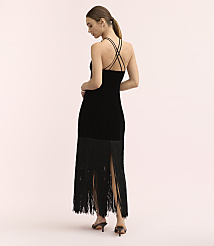A woman wearing a black velvet dress with a fringed hem stands against a plain, light pink background. carousel Product Image 3