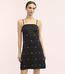 A woman wearing a black mini dress with small white embellishments stands against a plain light pink background. carousel Product Image 1