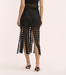 A woman stands with her back to the camera wearing a black lace skirt and heels against a plain light pink background. carousel Product Image 3