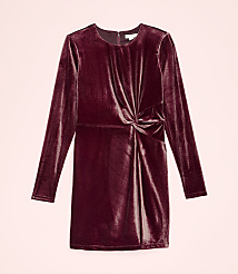 A long-sleeved, burgundy velvet dress with a knotted waist is centered against a plain light pink background. carousel Product Image 2