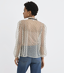 A woman wearing a sheer polka-dot blouse and blue jeans stands against a plain white background. carousel Product Image 3