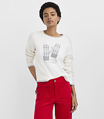 A woman wearing a white sweater with a mitten design and red pants stands against a plain white background. carousel Product Image 1