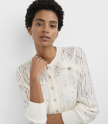 A woman with short curly hair wearing a white lace cardigan with a feather detail poses against a plain white background. carousel Product Image 2