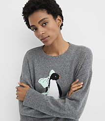 A woman with short curly hair wearing a grey sweater with a penguin graphic stands against a plain white background. carousel Product Image 1