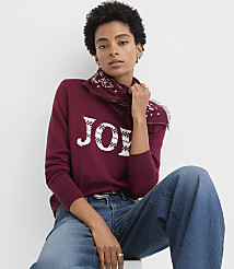 A woman wearing a burgundy "JOY" sweater and blue jeans poses against a plain white background. carousel Product Image 1