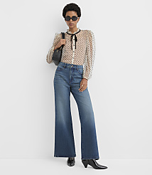A woman wearing a polka-dot blouse, wide-leg jeans, and sunglasses stands against a plain white background. carousel Product Image 2