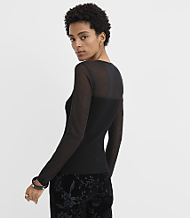 A woman wearing a sheer black long-sleeved top and floral velvet trousers poses against a plain white background. carousel Product Image 3