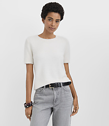 A woman wearing a white fuzzy short-sleeved sweater and grey jeans stands against a plain white background. carousel Product Image 1